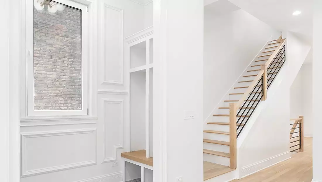 White Mud Room featuring Milled Wood Wall Panels and Brick Inlay, and Adjacent Staircase Contrasting Light Wood Steps